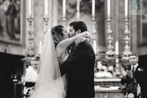 The bride and groom kiss in front of the cathedral altar.