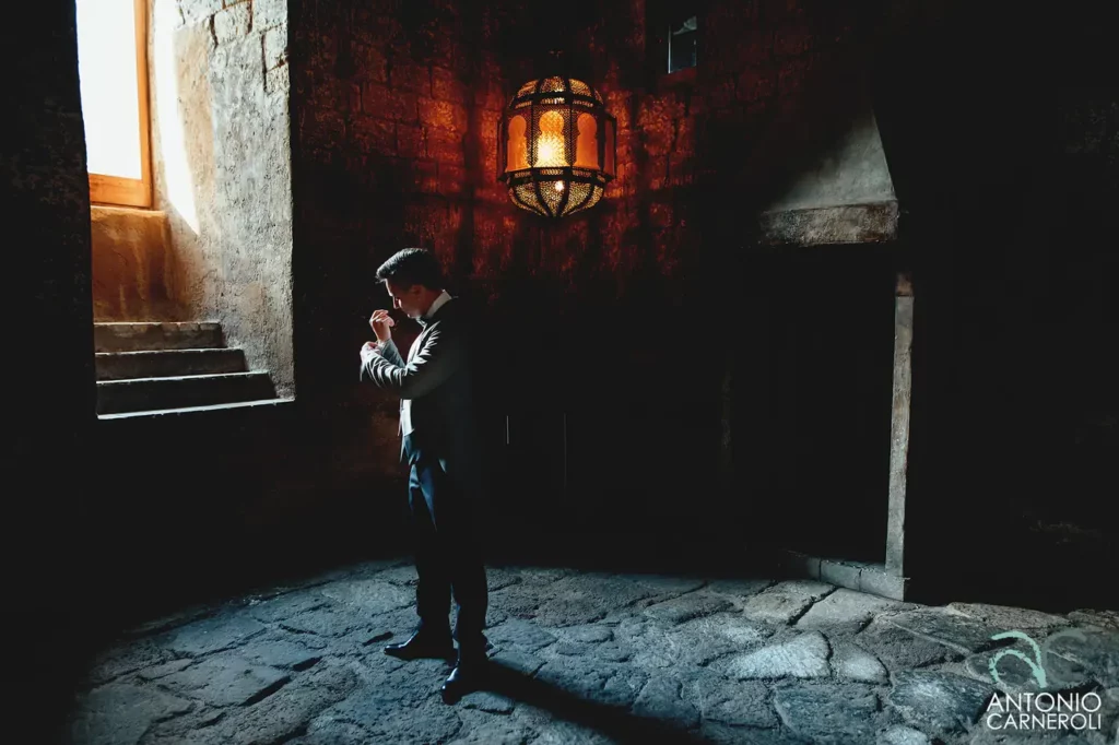 Lo sposo in piedi con una lanterna in una stanza buia durante il Matrimonio all'Abbazia di San Giusto.