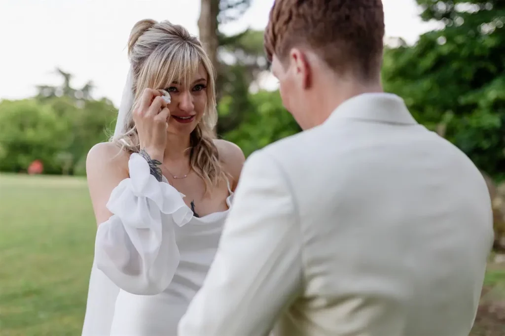 A bride wiping away a tear during a heartfelt moment with a man outdoors.