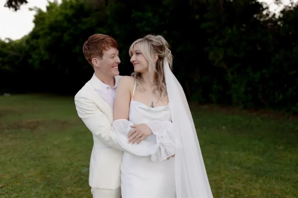 A newlywed couple smiling and embracing outdoors.