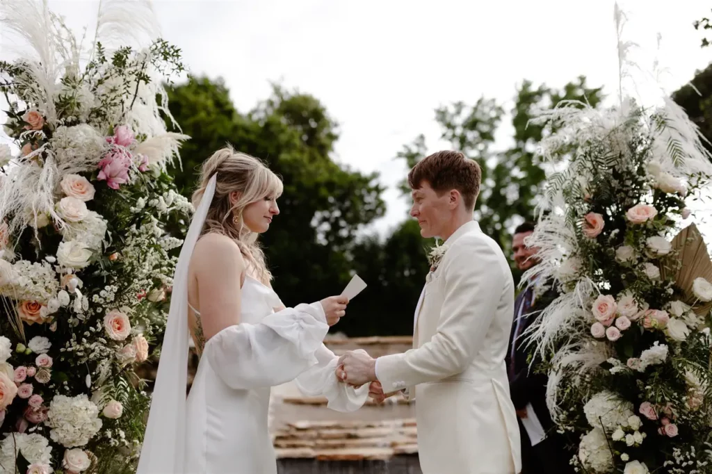 A couple exchanging wedding vows during an outdoor wedding ceremony surrounded by floral arrangements.