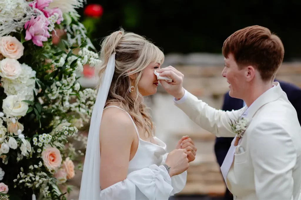 The groom gently wipes a tear from the bride's cheek during the wedding ceremony.