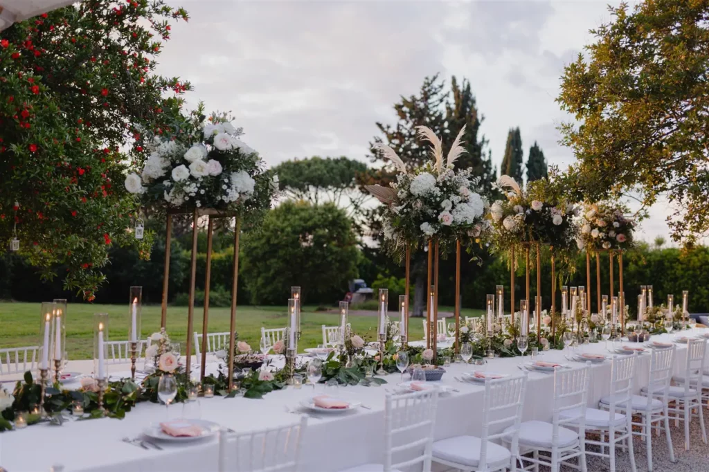 Elegant outdoor reception set-up with floral centerpieces and white chairs.