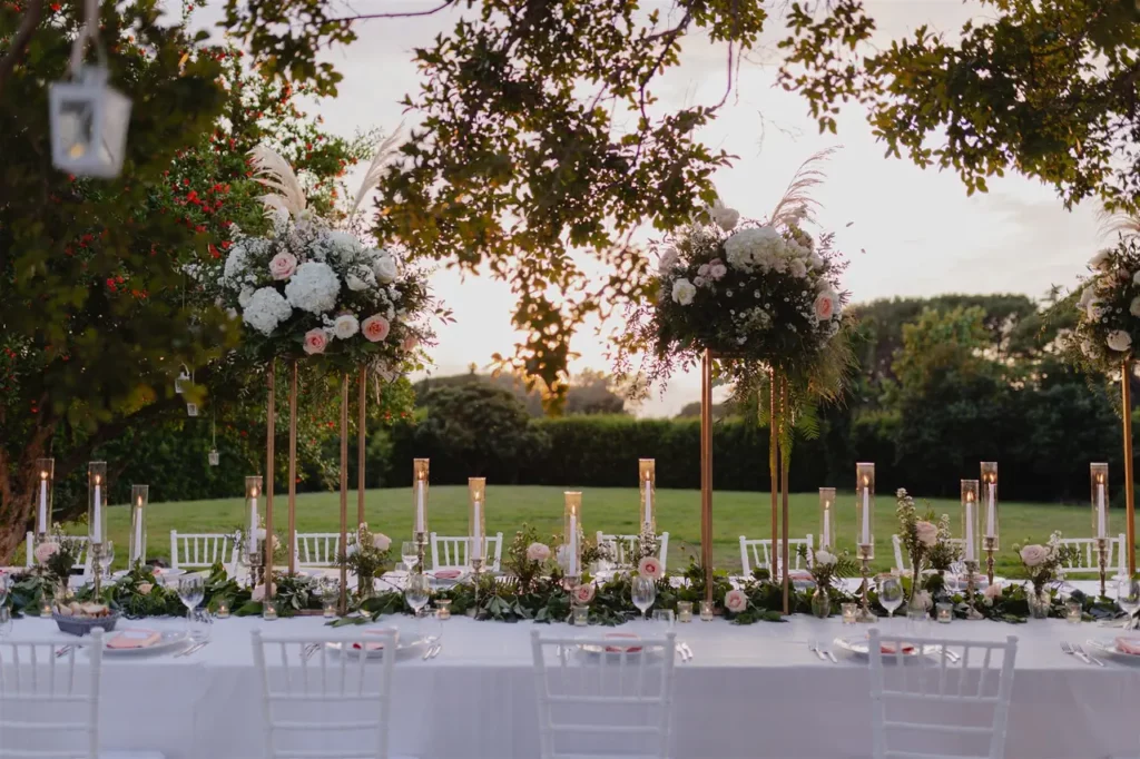 Elegant outdoor reception table at dusk with floral centerpieces and candles.