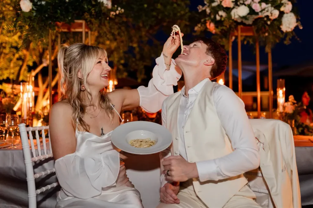 The bride jokingly gives the groom a bite to eat during an elegant outdoor evening.