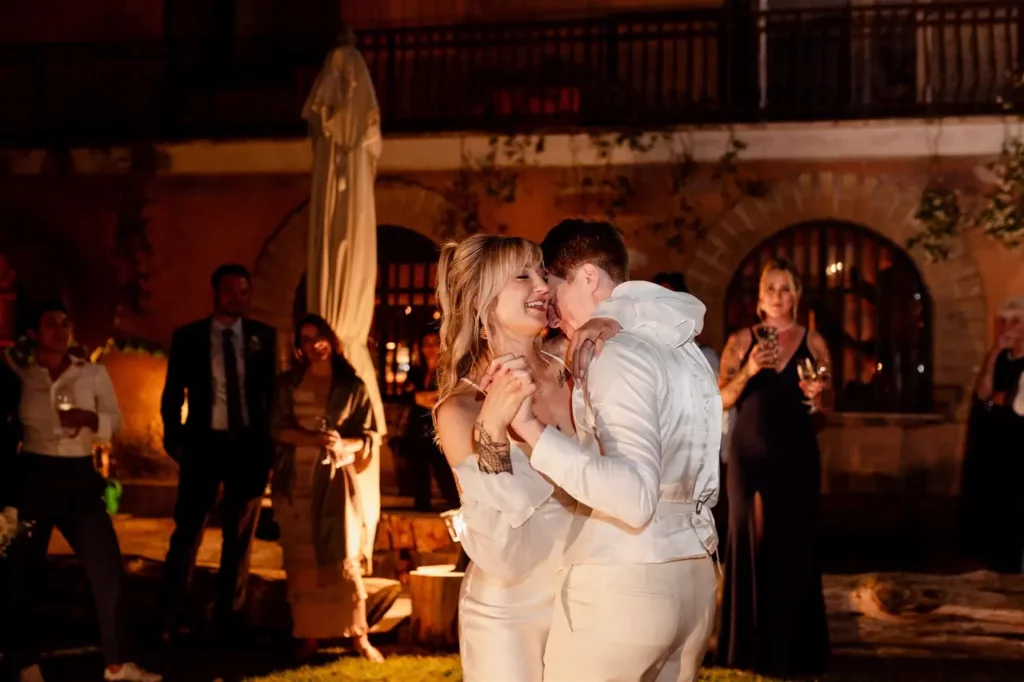 The bride and groom dance at the reception in an outdoor evening setting, surrounded by spectators.