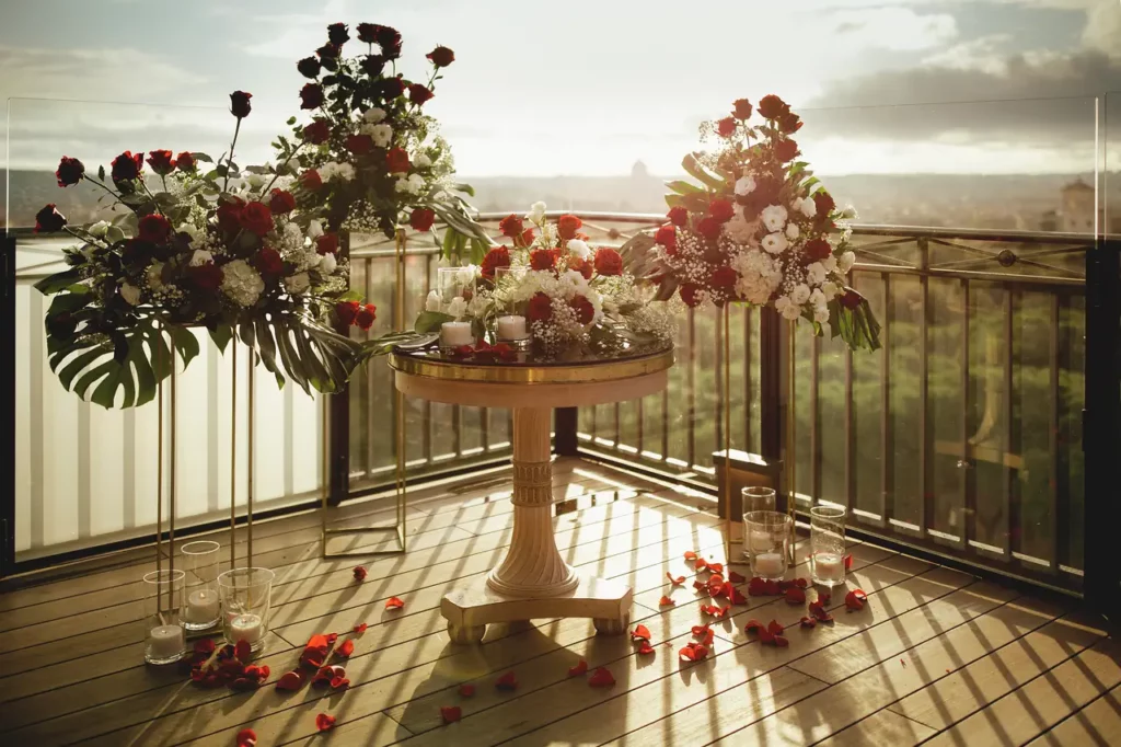 Elegant floral arrangements on round table with scattered petals against the backdrop of a sunny landscape seen from the adele terrace.