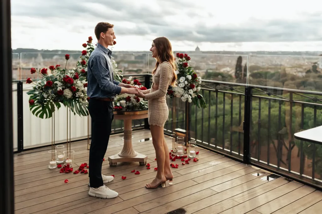 Couple holding hands in a romantic setting with flowers on a terrace overlooking rome.
