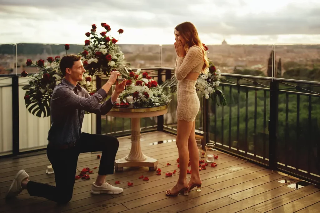 Un uomo in ginocchio fa una proposta di matrimonio a Roma ad una donna su un terrazza decorato con fiori e petali di rosa.