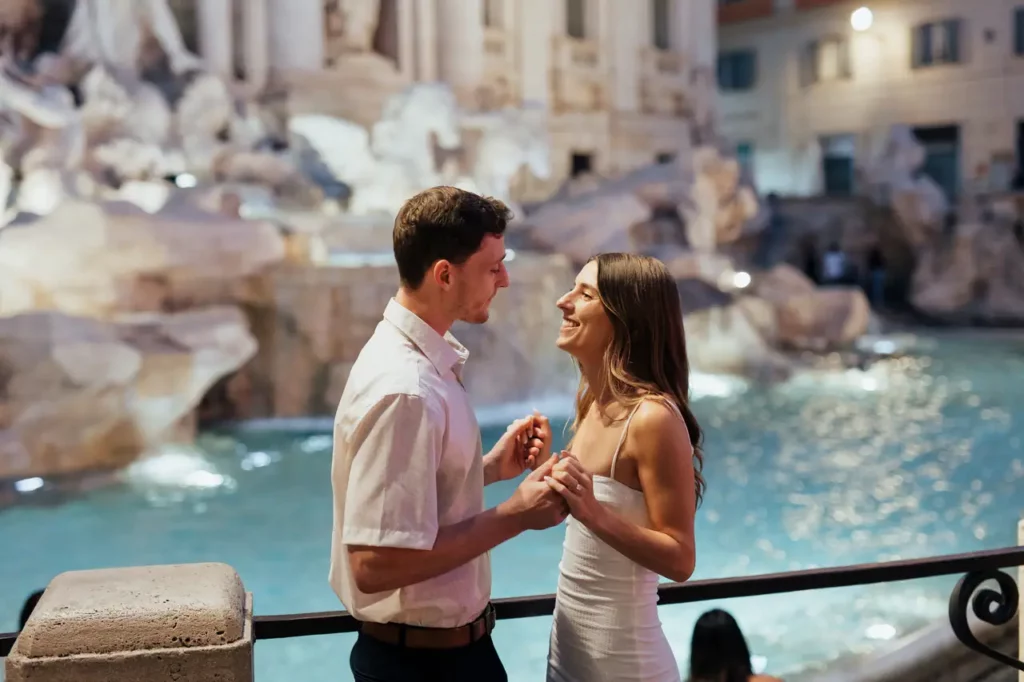 A couple holding hands at the Trevi Fountain in Rome at night.