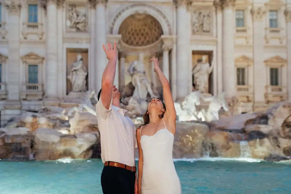 Couple tossing a coin into the Trevi Fountain at dawn.