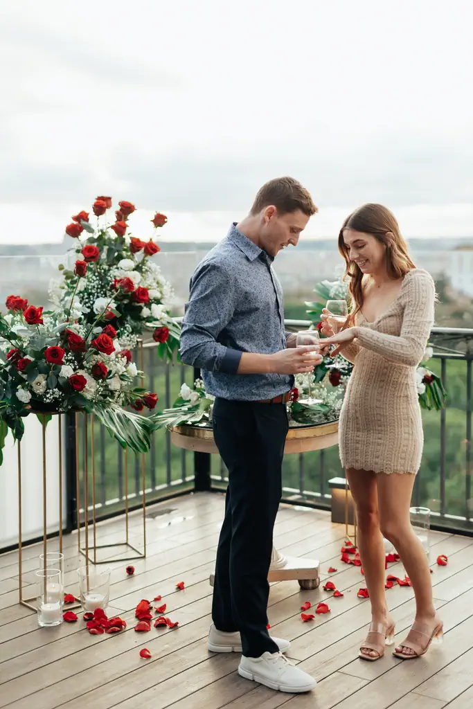 Two people celebrate with a toast on a terrace decorated with flowers in Rome.