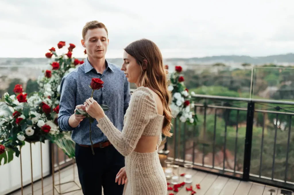 A man presents a rose to a woman on a terrace decorated with flowers.