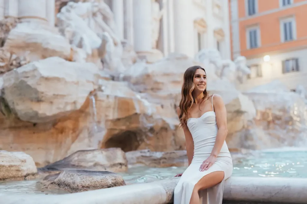 A woman in a white dress sitting next to the Trevi Fountain.