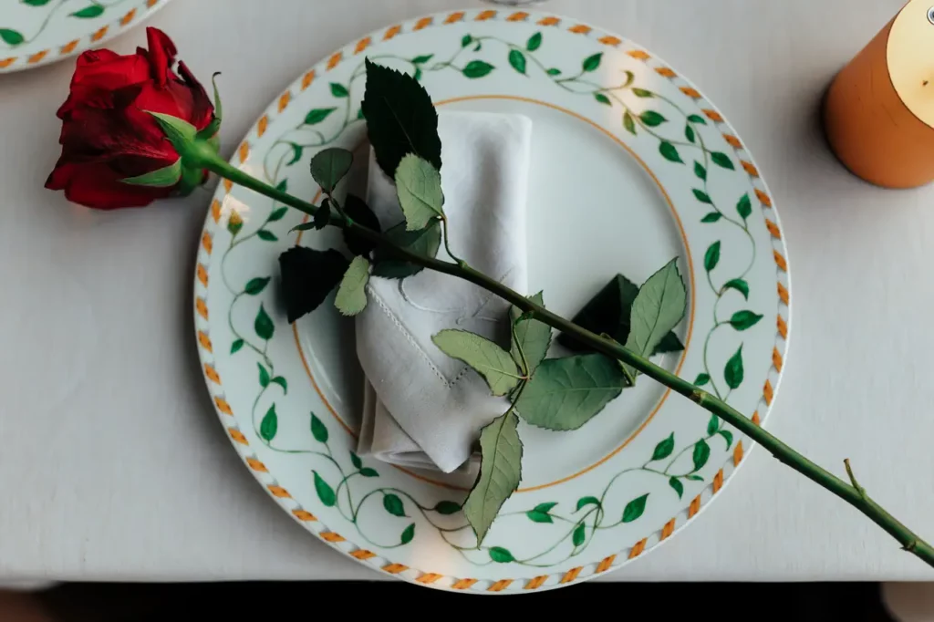 A red rose lying on a folded napkin on a decorative plate.