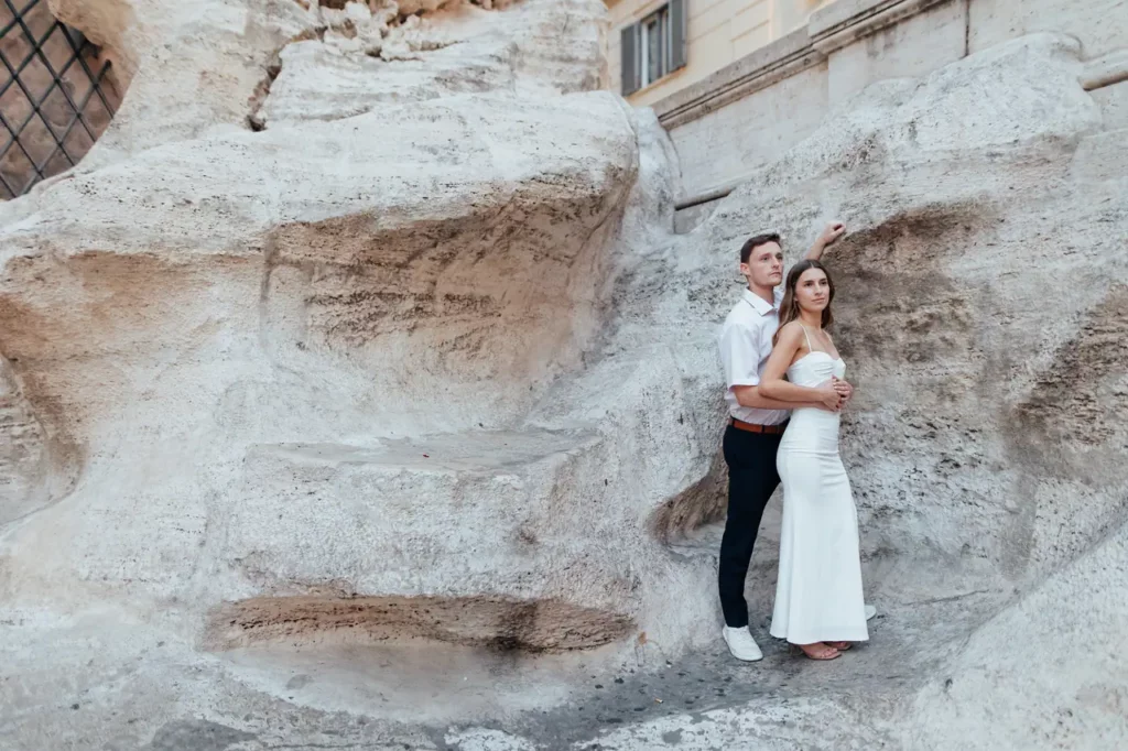 A couple in formal attire pose together against the stone backdrop of the Trevi Fountain.