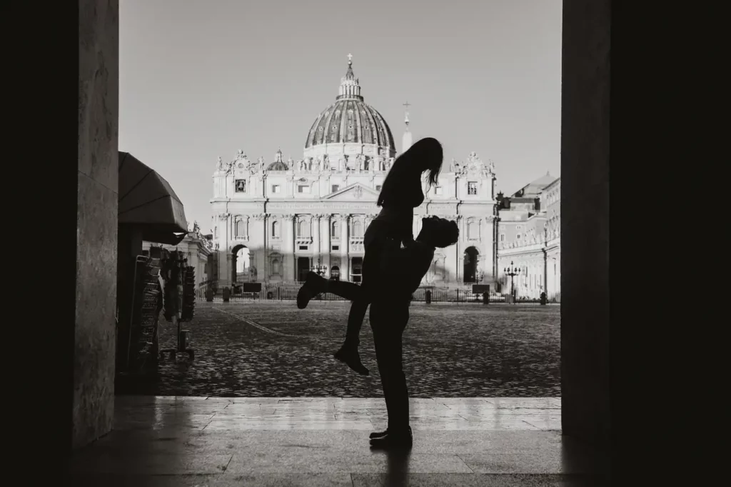 Silhouette of an embracing couple, with one person raised. The background shows a historic building with a dome, the majestic architecture of st. Peter's in vatican city.