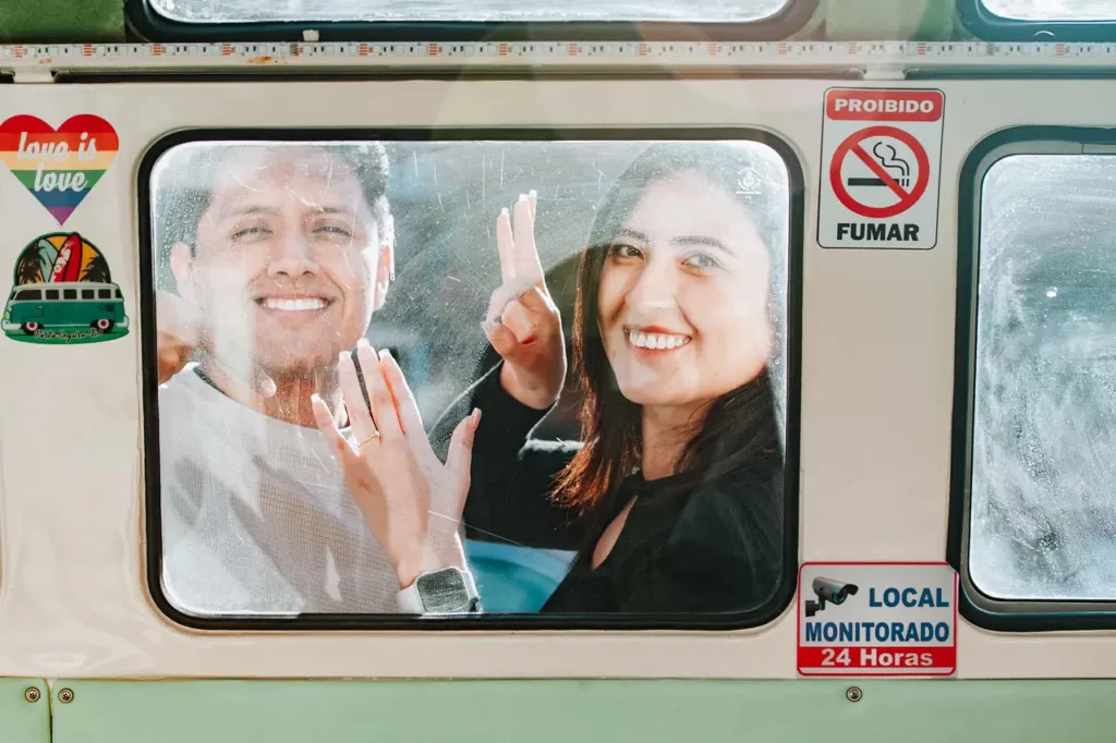 A smiling man and woman make through the window of a bus, with signs indicating no smoking.