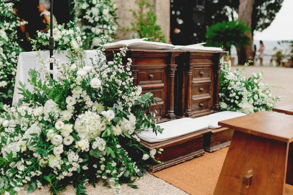 Ornate wooden chairs surrounded by lush white and green floral arrangements in an outdoor location evoke the timeless elegance of our lady of the most holy rosary church.