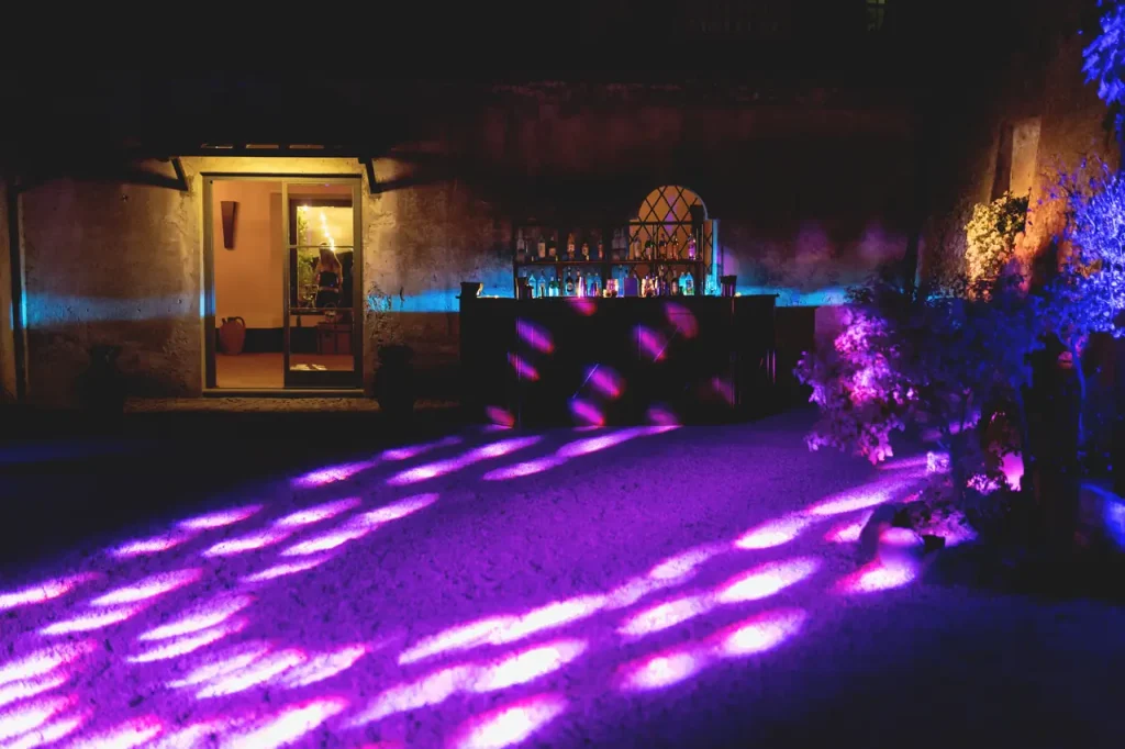 Purple and blue lights illuminate an open bar on the patio, creating a lively nighttime atmosphere.