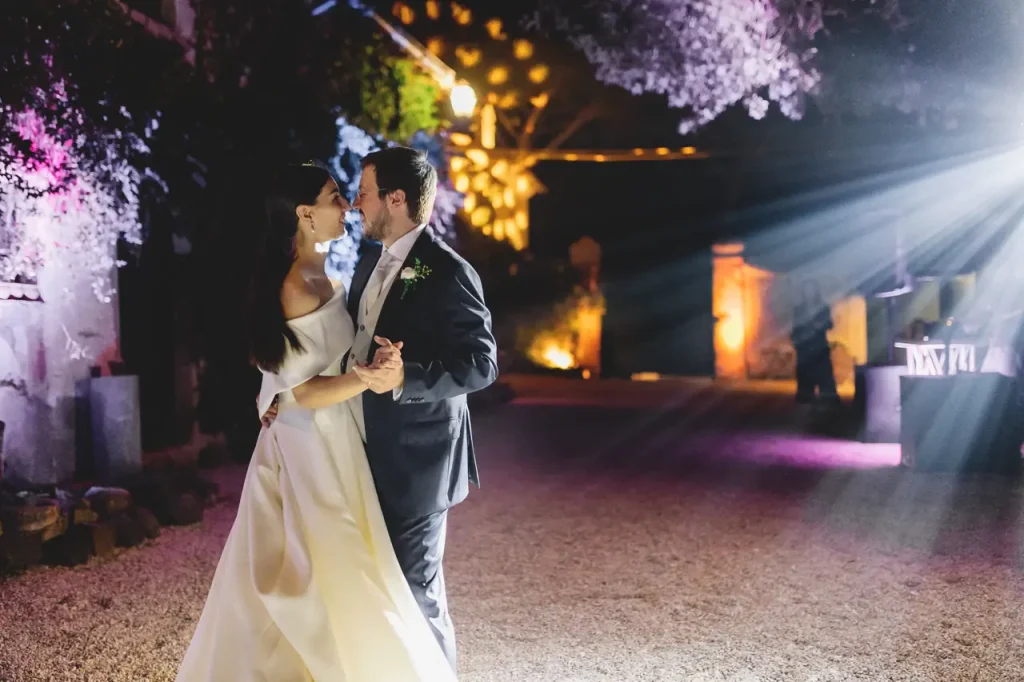 At night, the bride and groom dance close together outdoors, surrounded by colorful lights and shadows.
