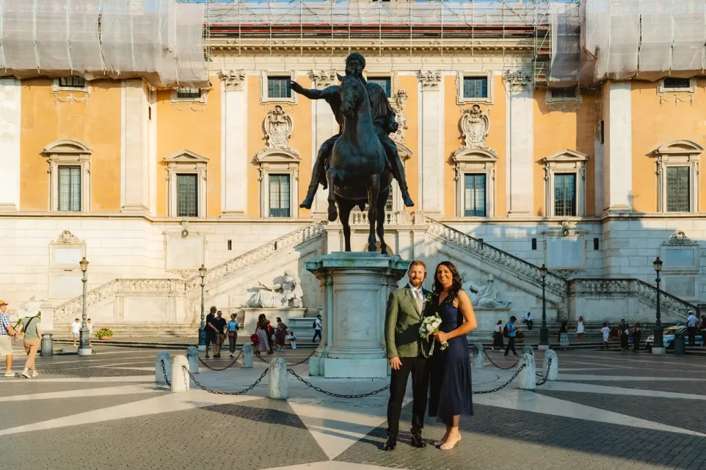 A couple poses for a photo in front of a bronze equestrian statue in capitol square, with a historic building and staircase elegantly framing the background.