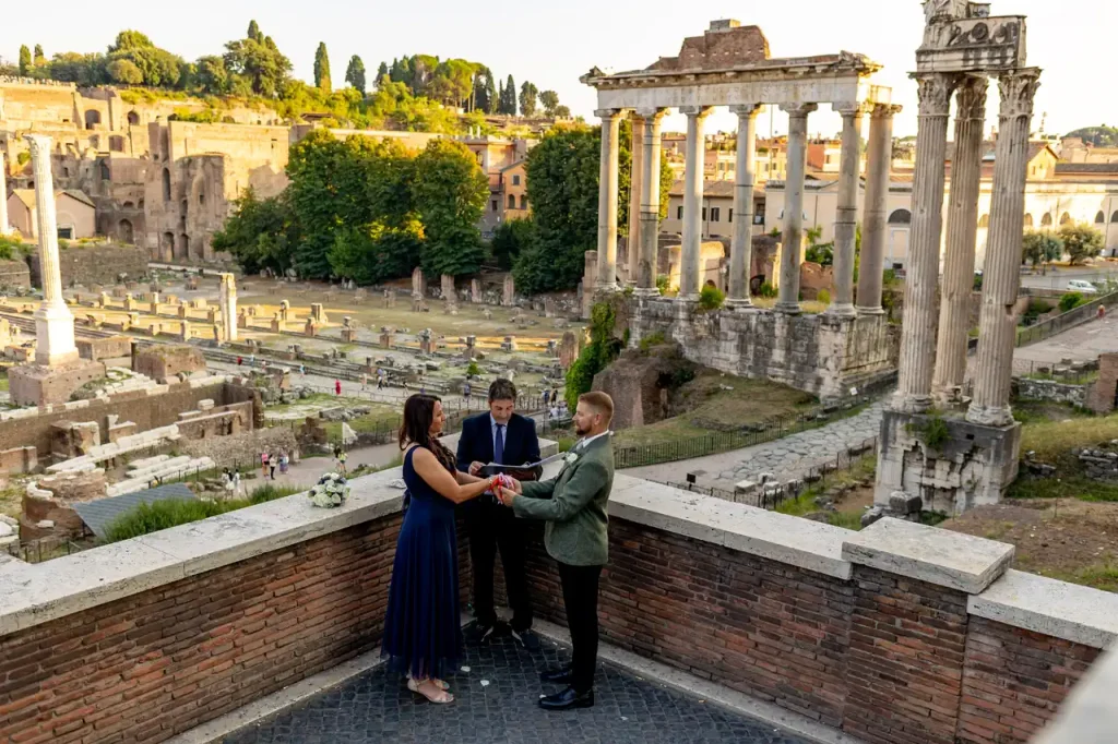A couple exchanges wedding vows with a celebrant during an enchanting outdoor wedding near the ancient ruins and majestic columns of the imperial fora.