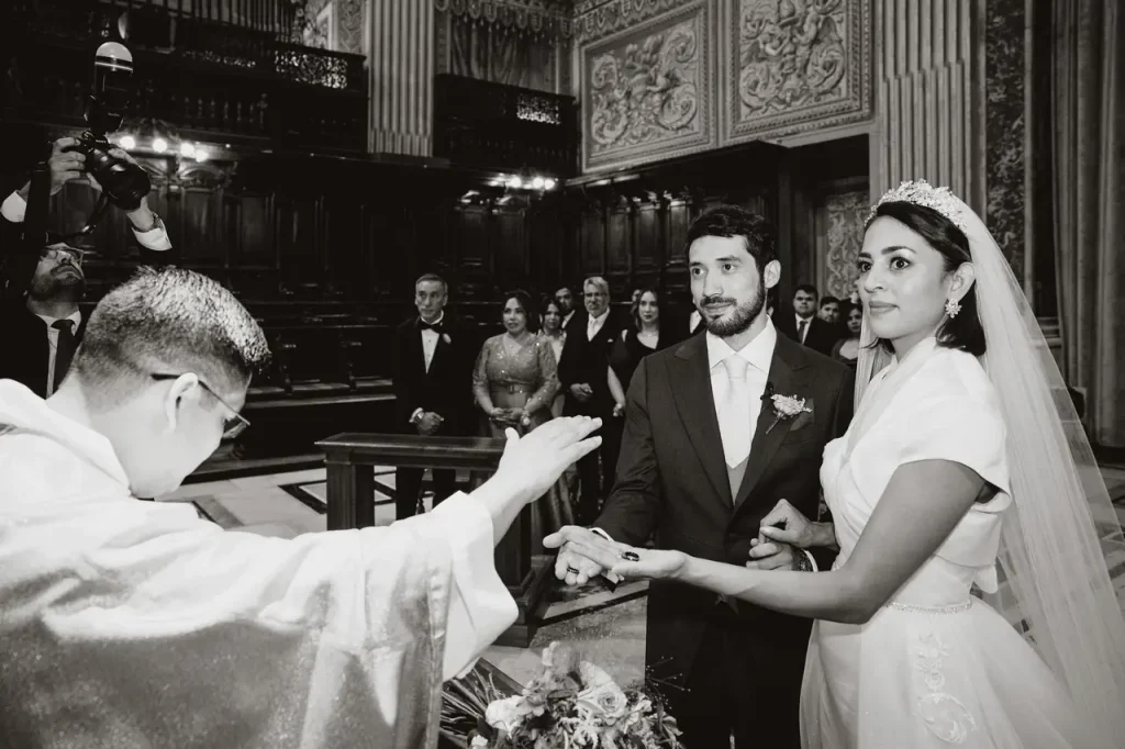 A priest performs a wedding ceremony as the bride and groom exchange rings in the vatican's richly decorated “choir chapel,” with guests seated in the background, creating the perfect atmosphere of a vatican wedding.