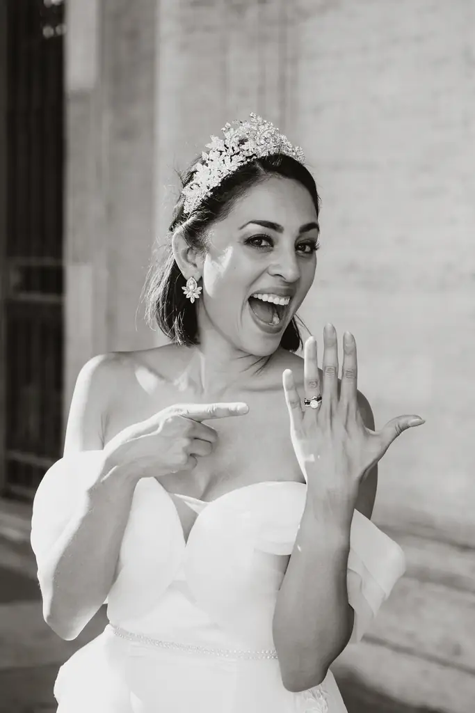 Vatican wedding: the story of gabriela and angel A woman in a wedding dress and tiara smiles and points to the ring on her finger, showing excitement after her wedding at the vatican.