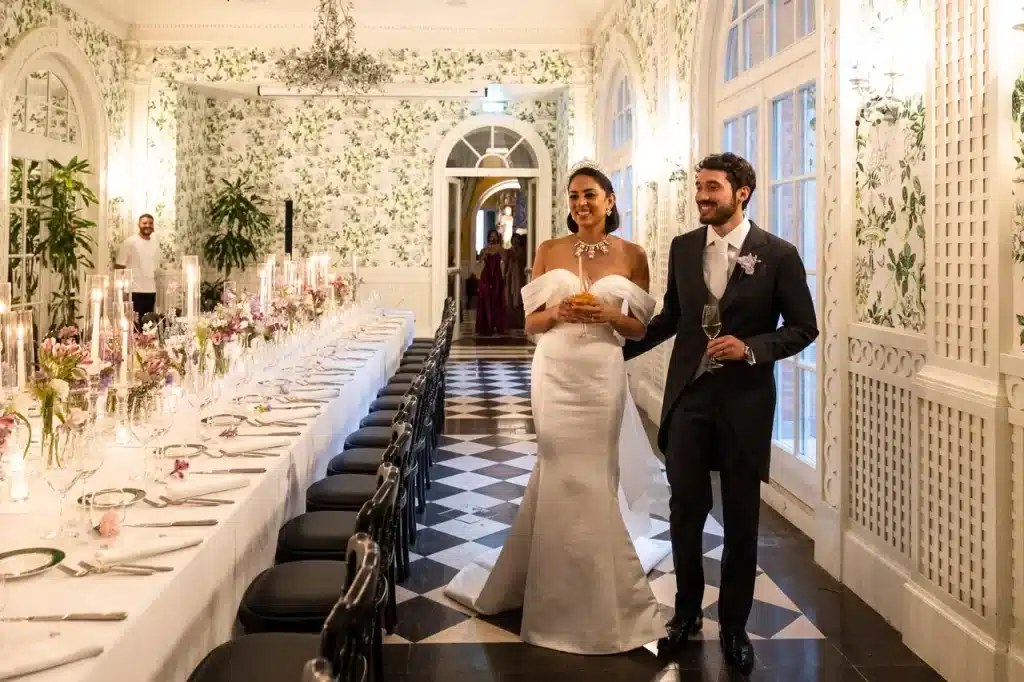 A married couple enters the ornate dining room of the hotel de la ville in rome, where a long banquet table set up awaits them.