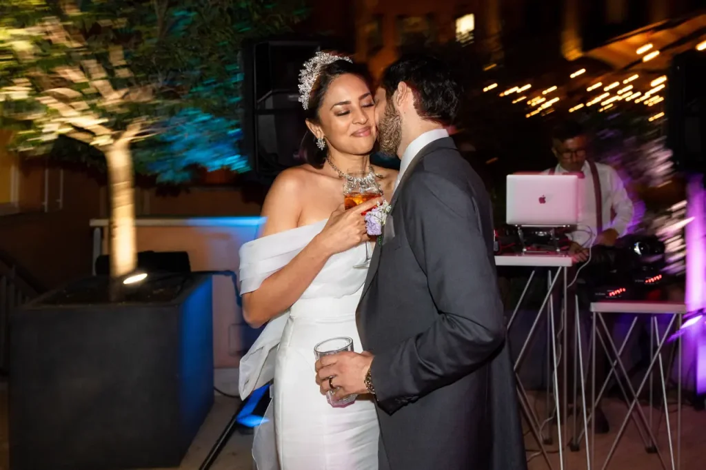 The bride and groom dance side by side during an outdoor wedding reception at the hotel de la ville in rome, sipping drinks and with a dj and string lights illuminating the backdrop.