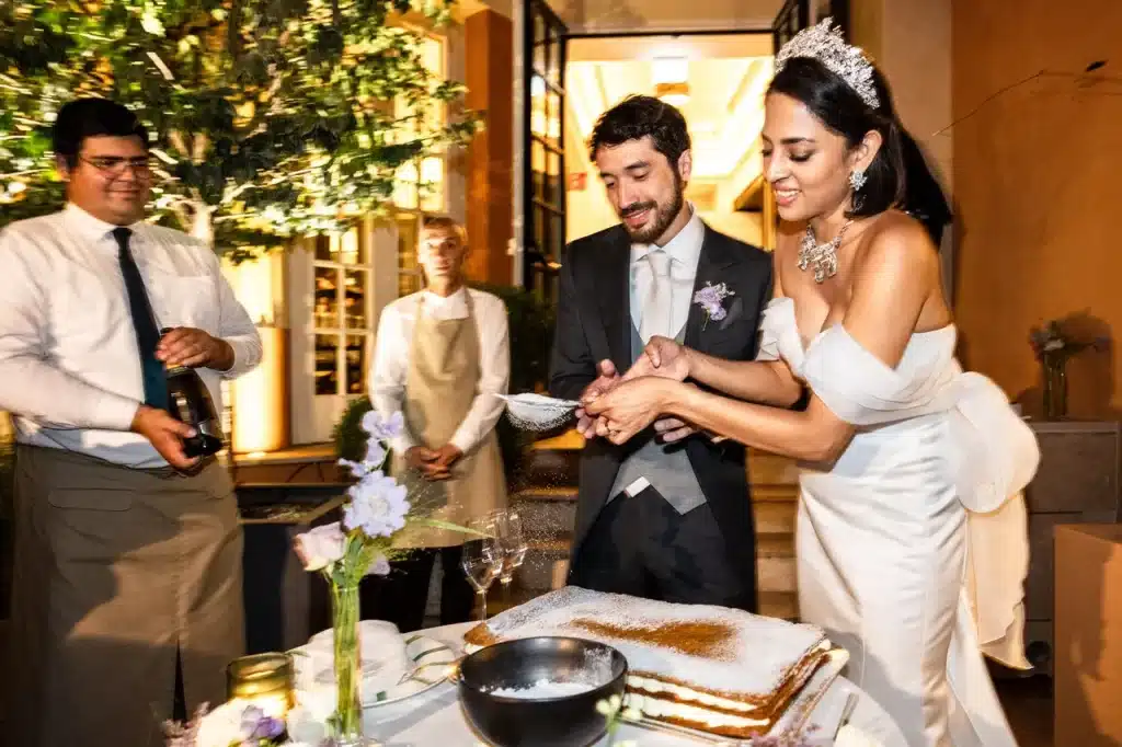 At their wedding in rome, the couple decorate a rectangular cake together during the reception, while two staff members watch in the background.
